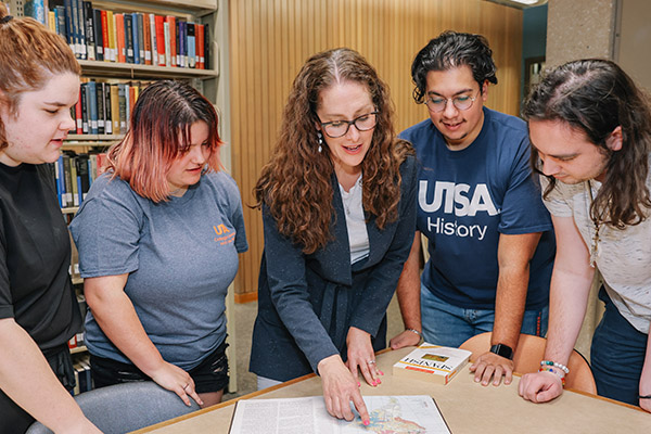 Professor surrounded by students as she goes over information in a textbook