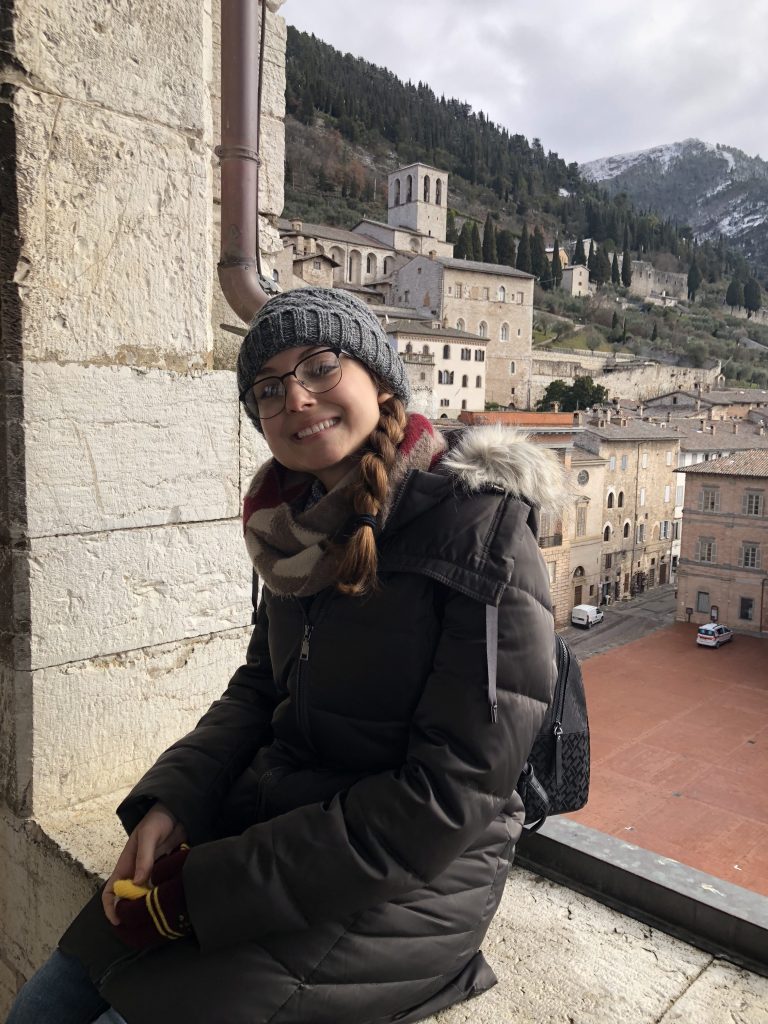 student smiling on a window ledge with a view of Gubbio, Italy