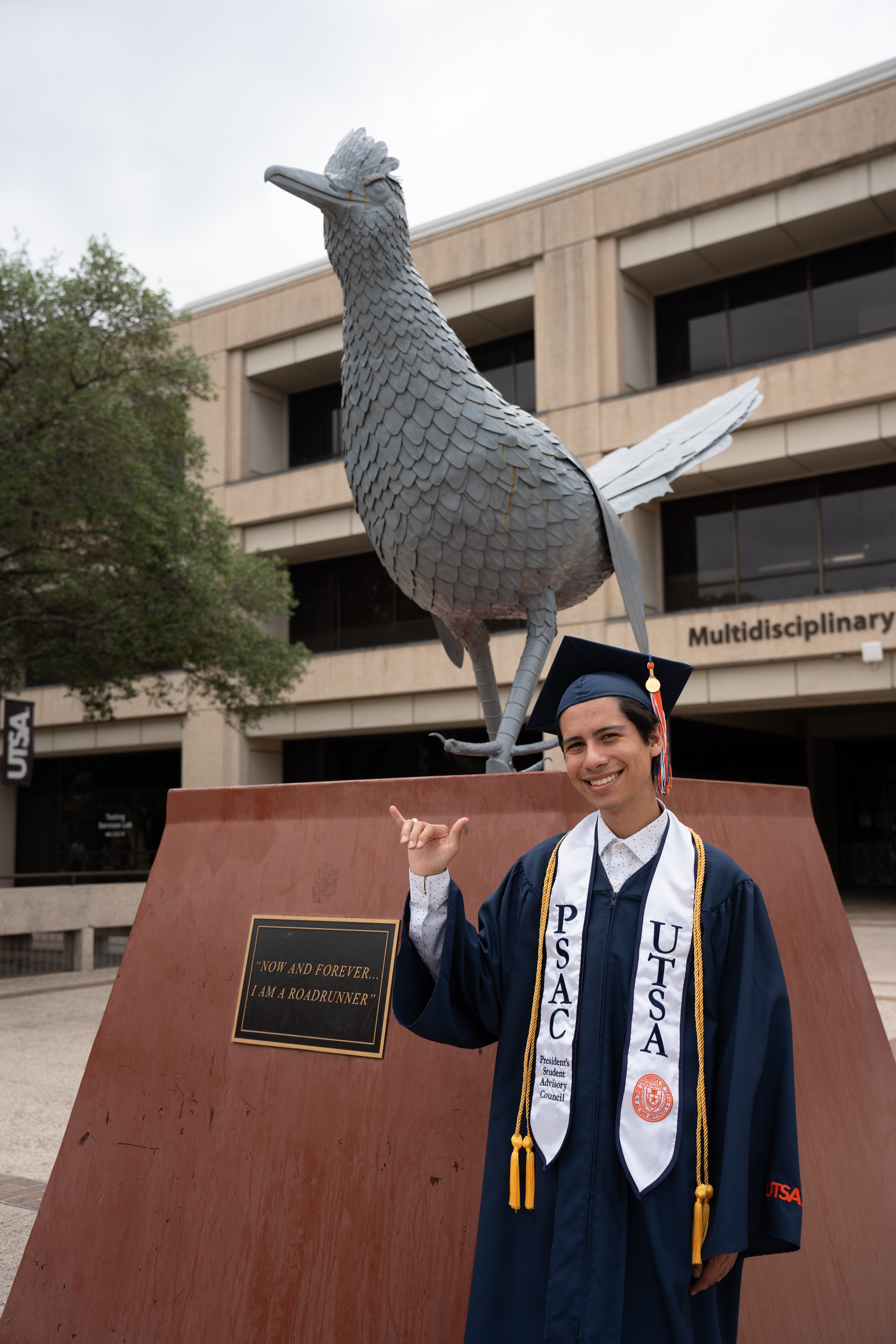SGA Aydan Villarreal in full commencement regalia in front of the Rowdy Statue